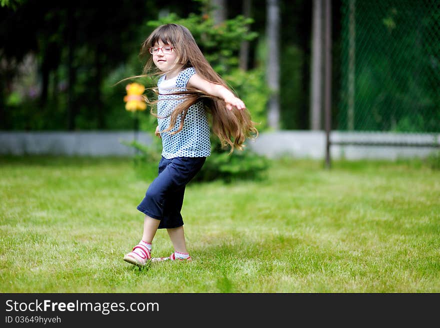 Adorable active little girl with long dark hair plays on backyard in spring