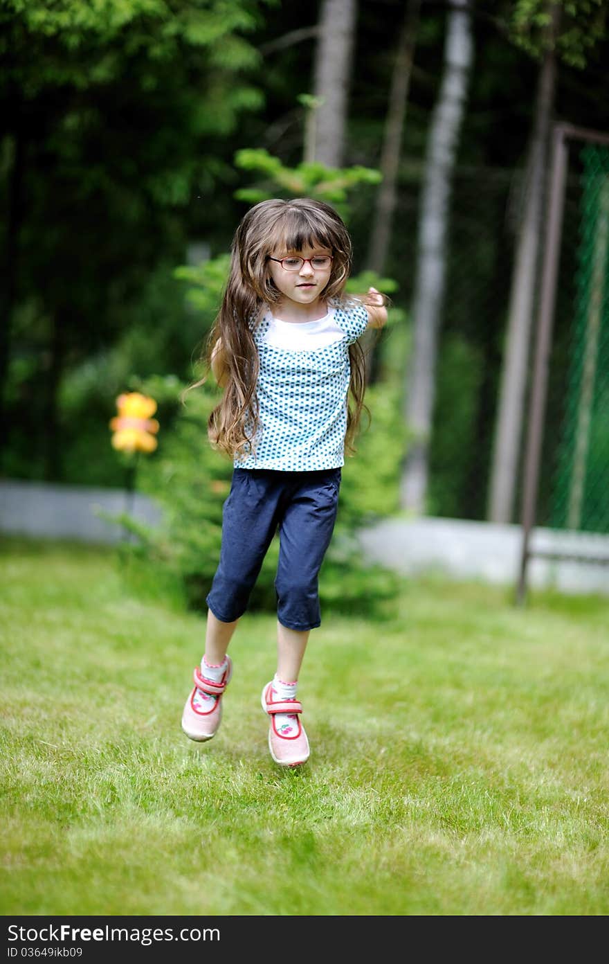 Adorable active little girl with long dark hair plays on backyard in spring