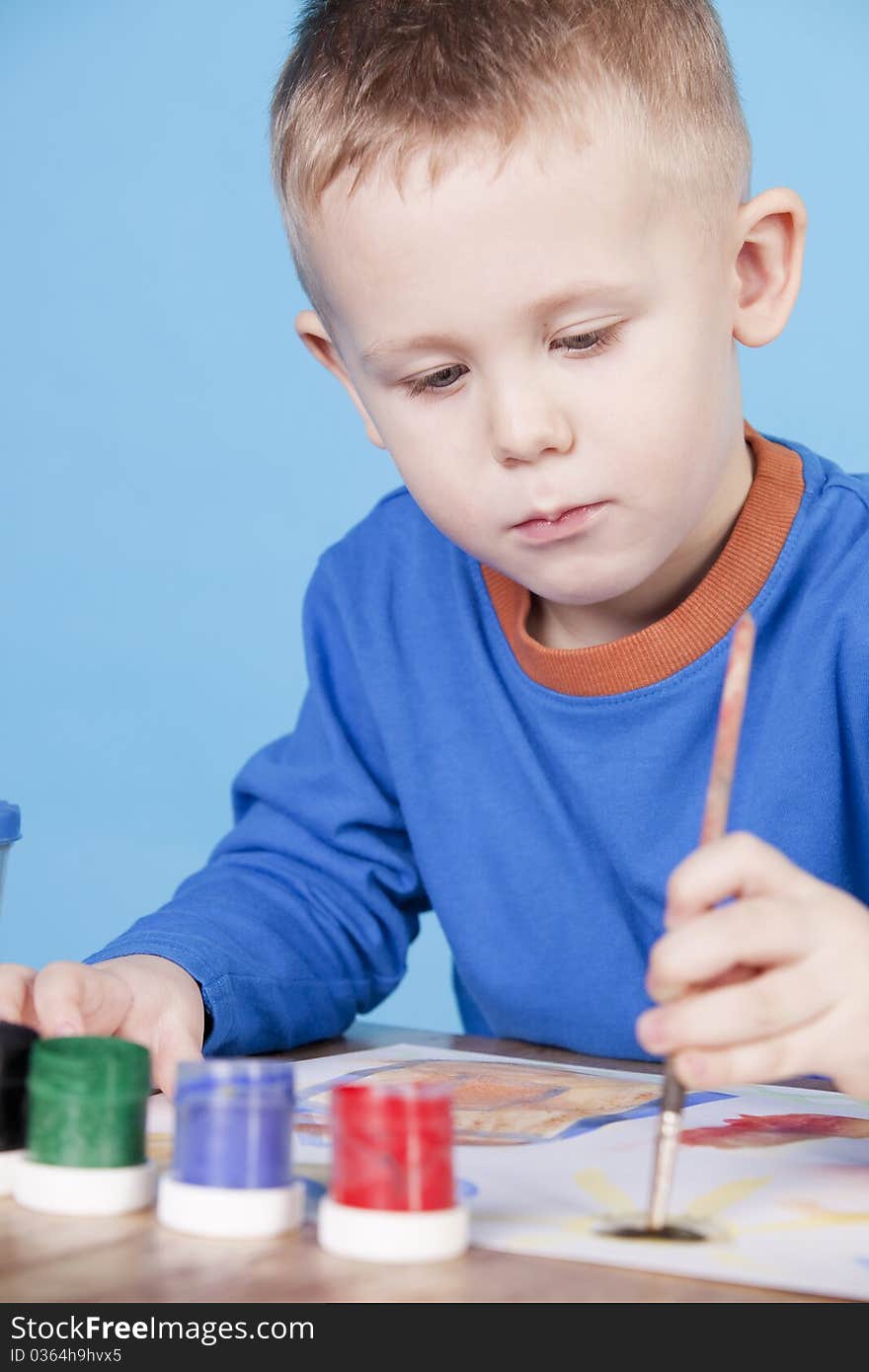 Thoughtful little boy draws pictures, on blue background