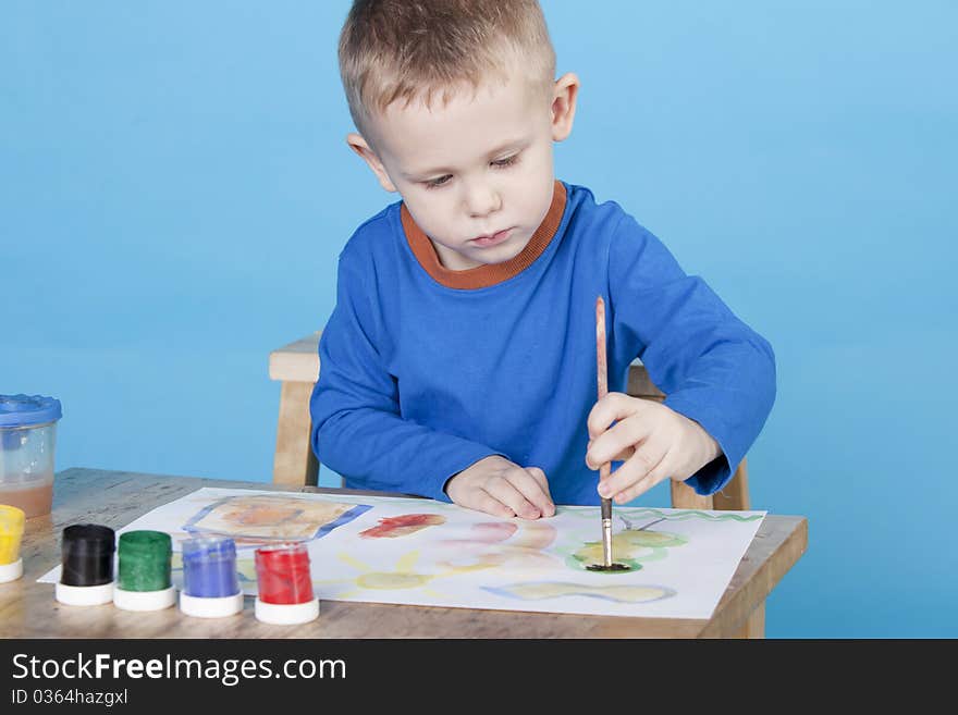 Beautiful thoughtful boy draws pictures on blue background