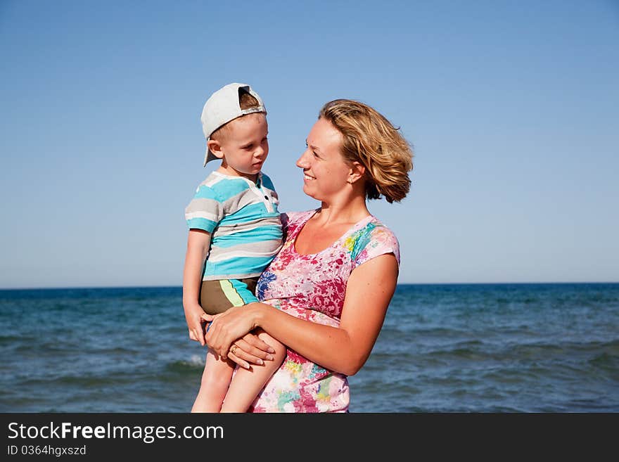 Beautiful mum holds the son on hands and looks at it on seacoast. Beautiful mum holds the son on hands and looks at it on seacoast