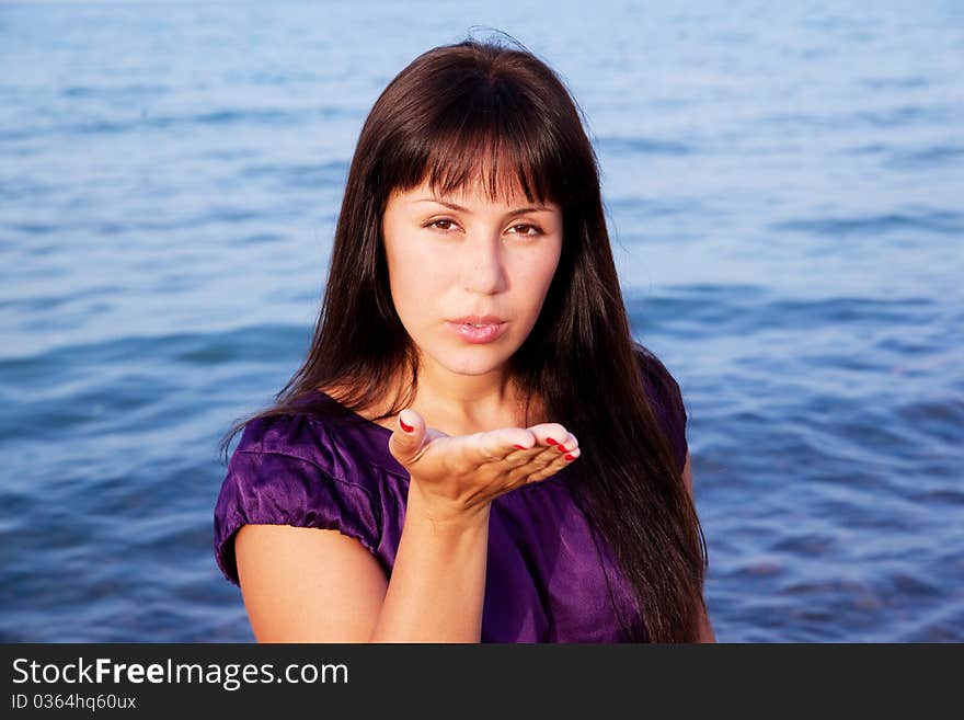 Beautiful girl sends an air kiss, blows on a palm, on sea background. Beautiful girl sends an air kiss, blows on a palm, on sea background