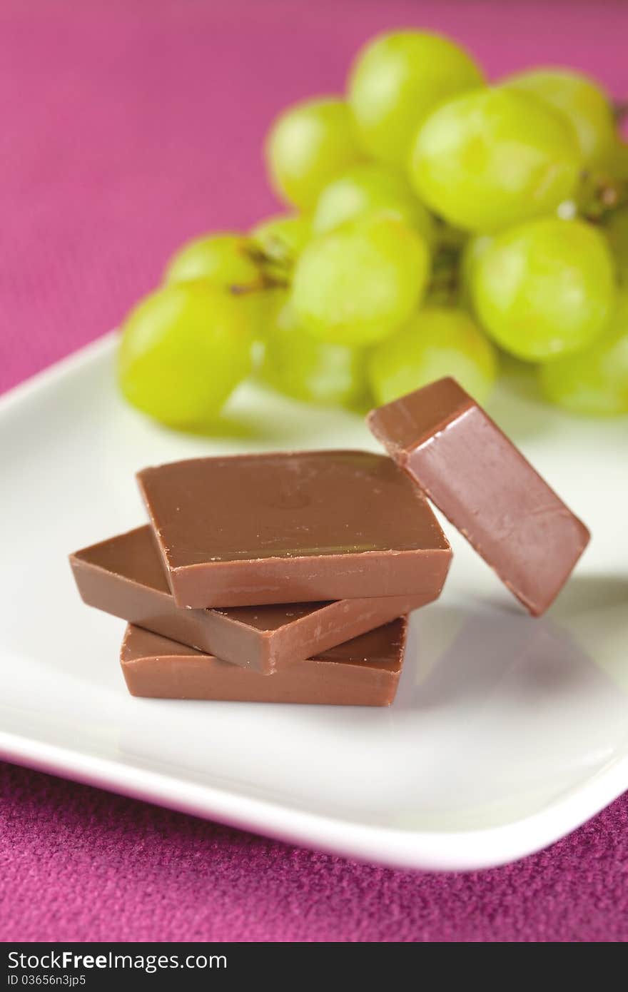 Chocolate pieces stacked on plate with grapes. Chocolate pieces stacked on plate with grapes