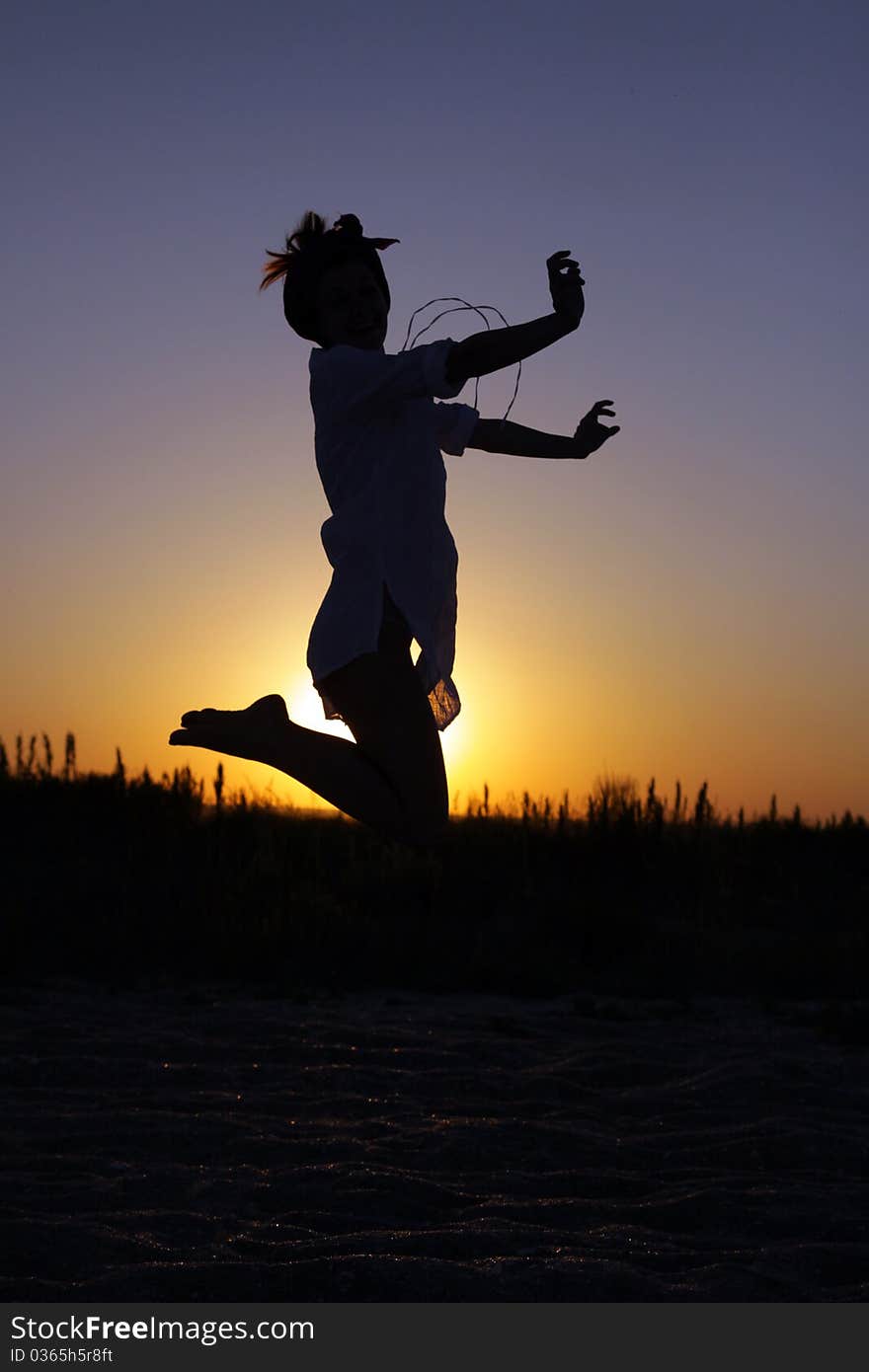 Silhouette of a young woman whearing a bandana and jumping at the sunset. Silhouette of a young woman whearing a bandana and jumping at the sunset