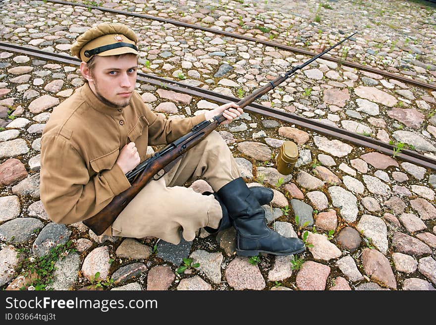 Soldier with gun and boiler in uniform of World War I, sit down and resting on the pavement. Costume accord the times of World War I. Photo made at cinema city Cinevilla in Latvia. Cockade on the hat do not contain trade mark. Soldier with gun and boiler in uniform of World War I, sit down and resting on the pavement. Costume accord the times of World War I. Photo made at cinema city Cinevilla in Latvia. Cockade on the hat do not contain trade mark.