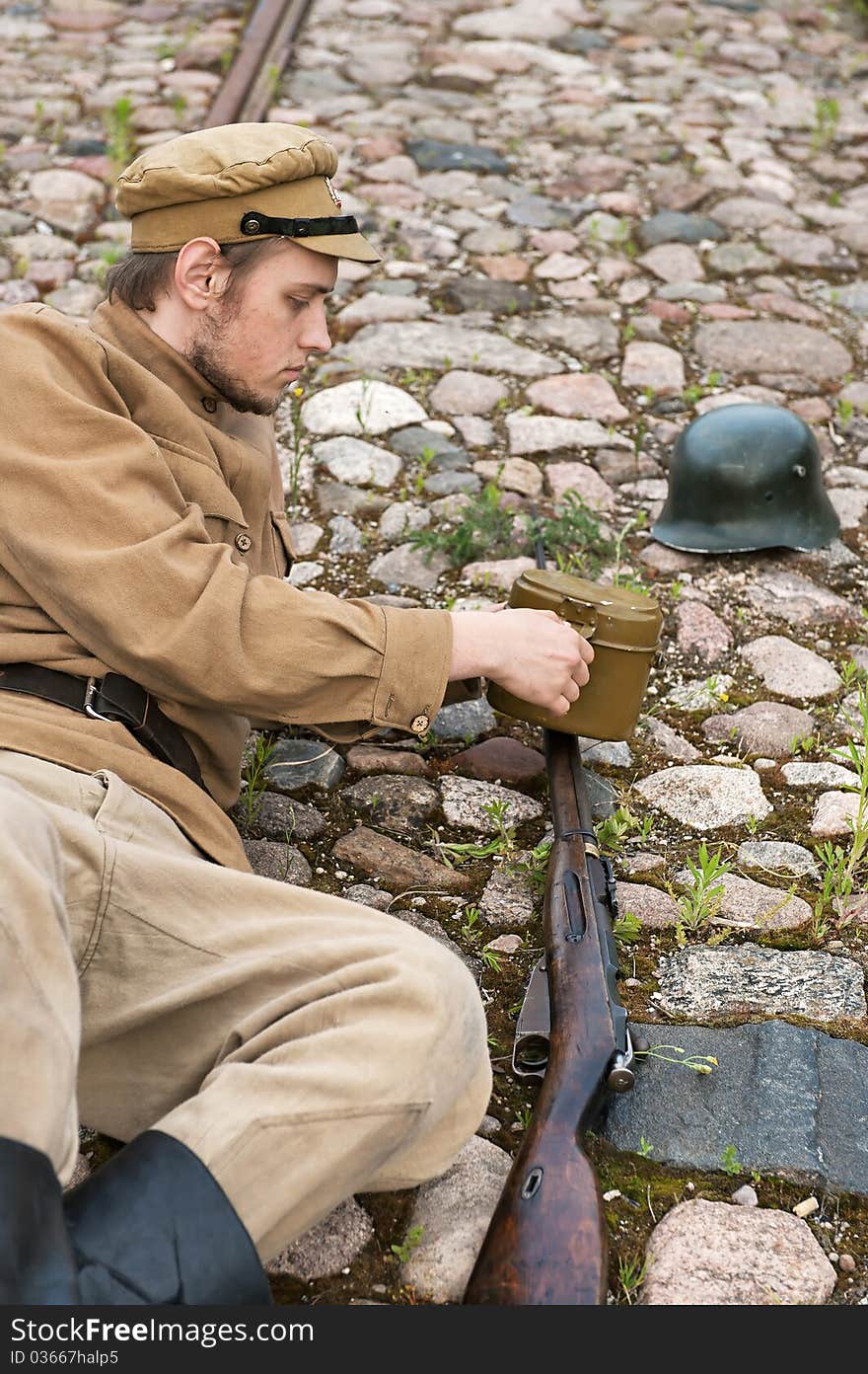 Soldier with gun and boiler in uniform of World War I, resting on the pavement. Costume accord the times of World War I. Photo made at cinema city Cinevilla in Latvia. Soldier with gun and boiler in uniform of World War I, resting on the pavement. Costume accord the times of World War I. Photo made at cinema city Cinevilla in Latvia.