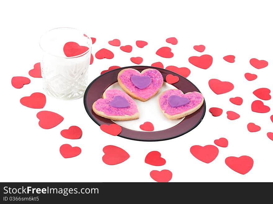 An angled closeup of a plate of homemade valentine cookies and a glass of milk with a valentine heart floating on top on a white isolated background. An angled closeup of a plate of homemade valentine cookies and a glass of milk with a valentine heart floating on top on a white isolated background.