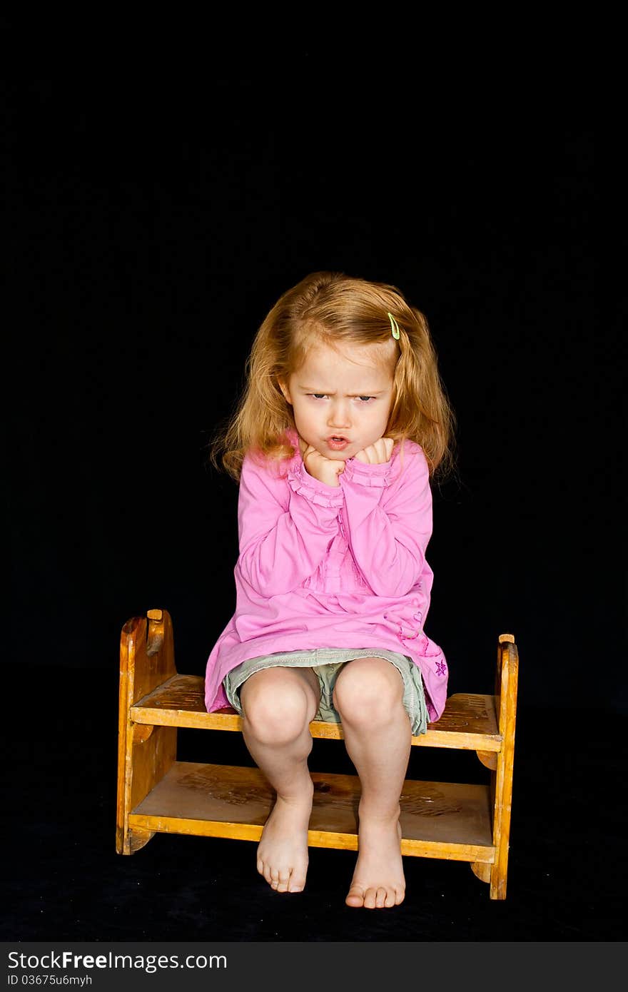 A cute girl sitting on a chair/stool. She has a very unique facial expression. She is pouting and thinking. A cute girl sitting on a chair/stool. She has a very unique facial expression. She is pouting and thinking.