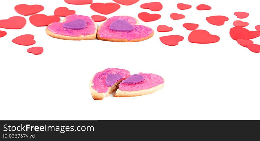 A front angled macro view of a couple a broken valentine cookie with couple of cookies in the back within a sea of valentines on an isolated white background. A front angled macro view of a couple a broken valentine cookie with couple of cookies in the back within a sea of valentines on an isolated white background.