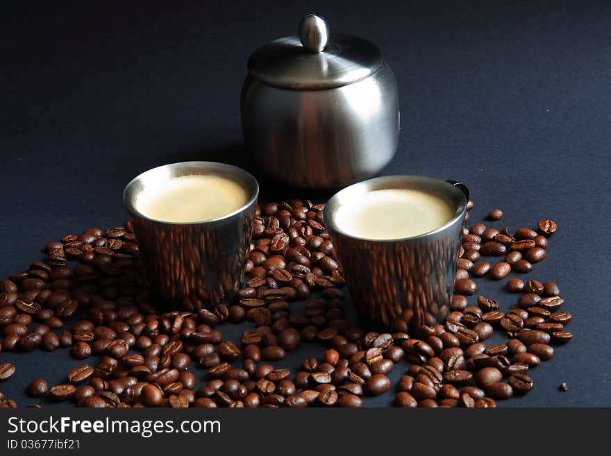 Coffee in metal cup and roasted beans on black background.