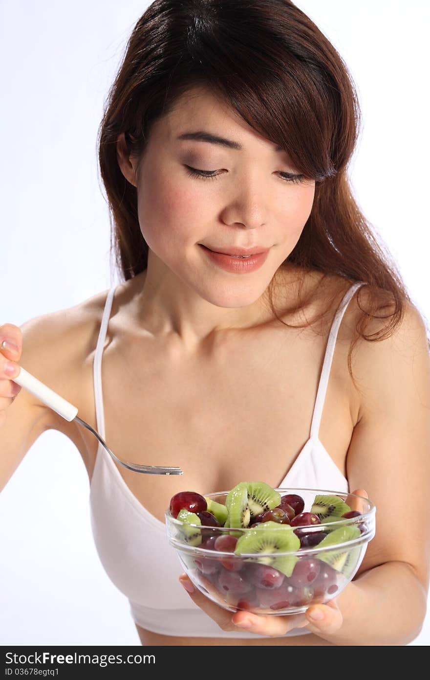 Close up of beautiful, young oriental girl, wearing sports underwear, while eating a fruit salad. Close up of beautiful, young oriental girl, wearing sports underwear, while eating a fruit salad.
