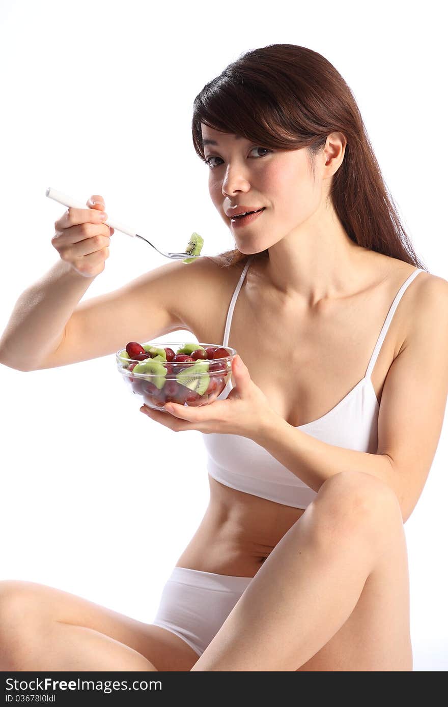 Beautiful, young oriental girl, wearing sports underwear, sitting down while eating a fruit salad. Beautiful, young oriental girl, wearing sports underwear, sitting down while eating a fruit salad.