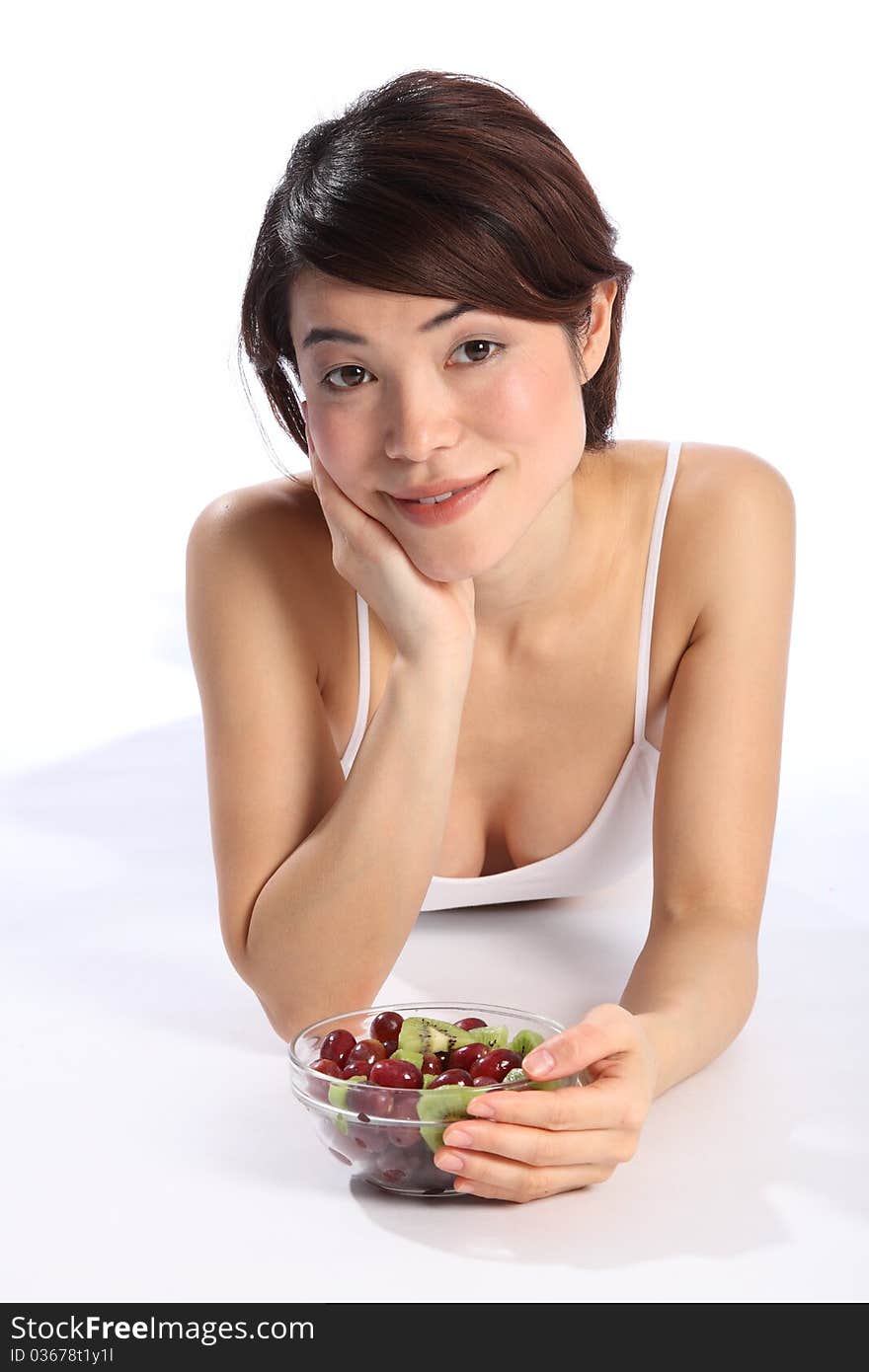 Close up portrait of beautiful, young oriental girl, lying on the floor with a bowl of kiwi and grape fruit. Close up portrait of beautiful, young oriental girl, lying on the floor with a bowl of kiwi and grape fruit.