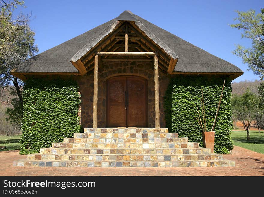 Stone chapel with thatch roof covered in green ivy against blue sky