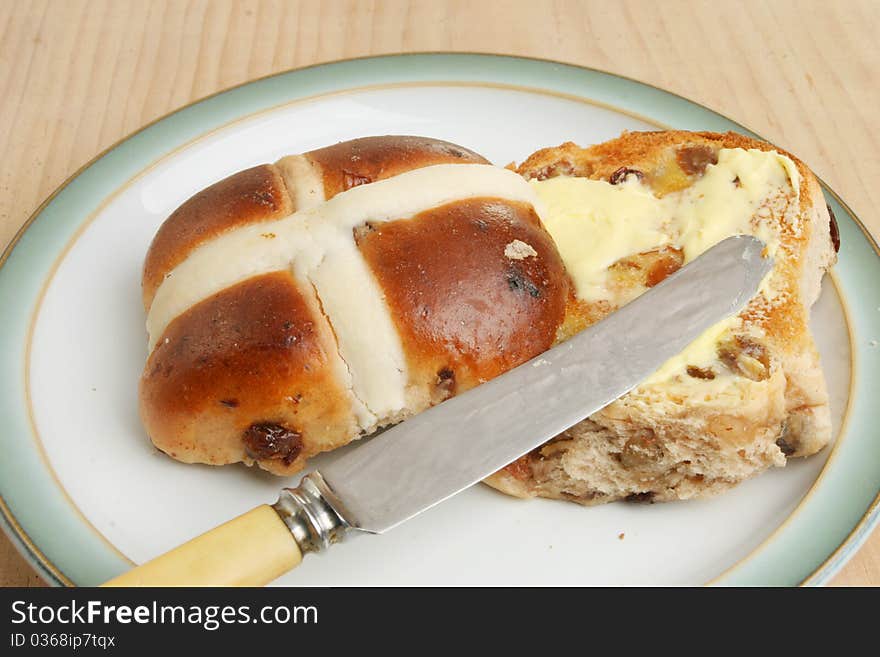 Toasted and buttered hot cross bun with a knife on a plate