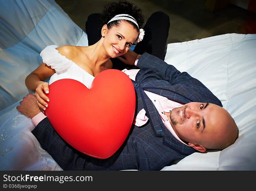 Joyful bride and groom with red toy heart