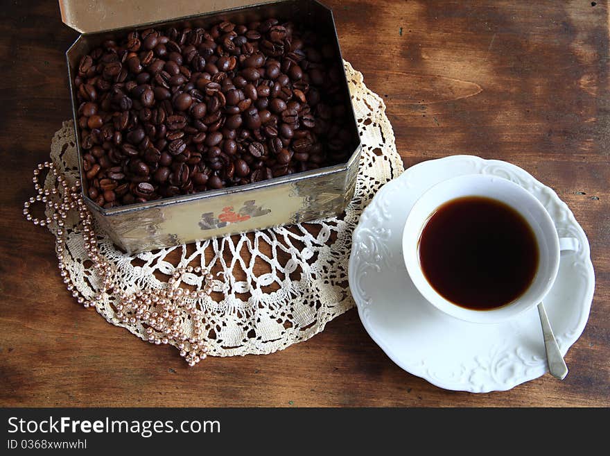 Coffee in white cup and box with roasted grain on wooden background.