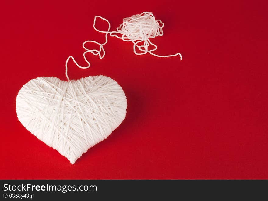 White heart made of wool on a red background. Valentine's Day.