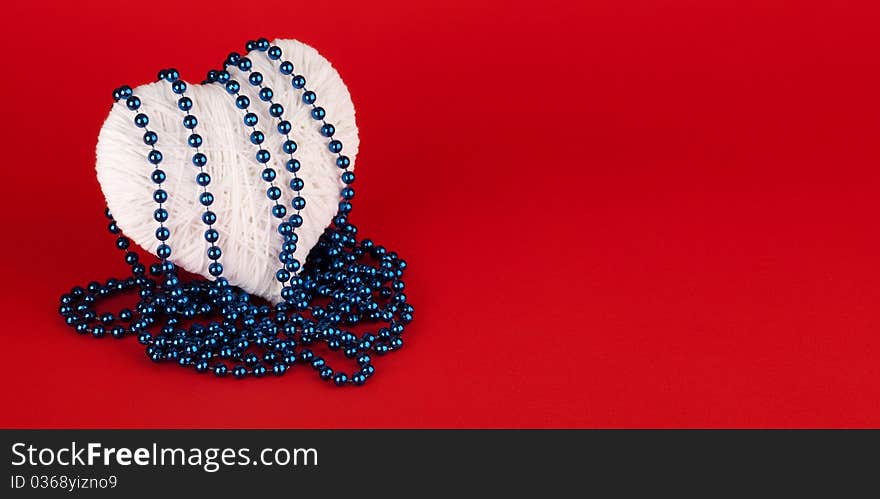 Beads on a white heart made of wool on a red background. Valentine's Day.