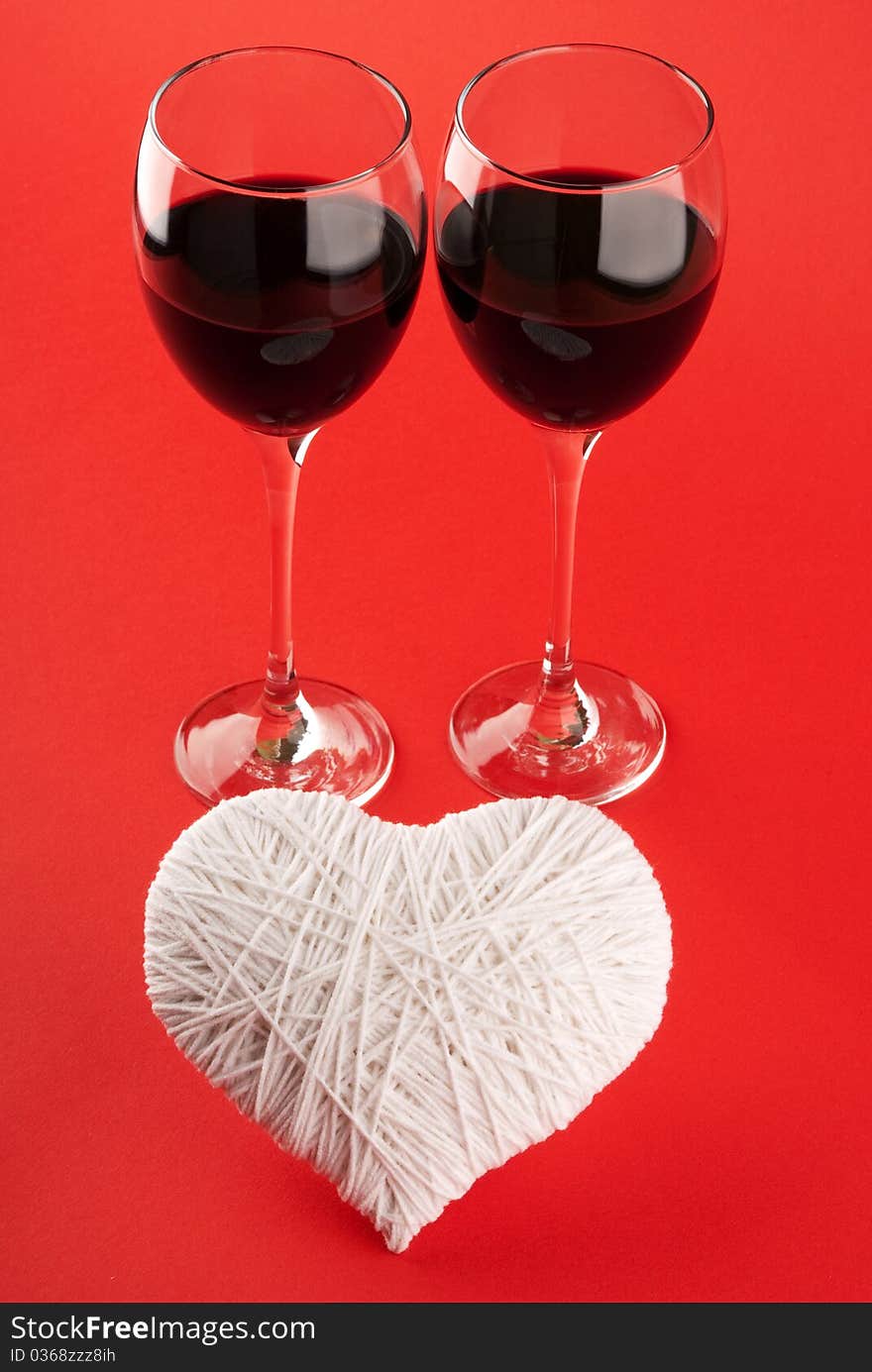 Two glasses of wine and a white heart made of wool