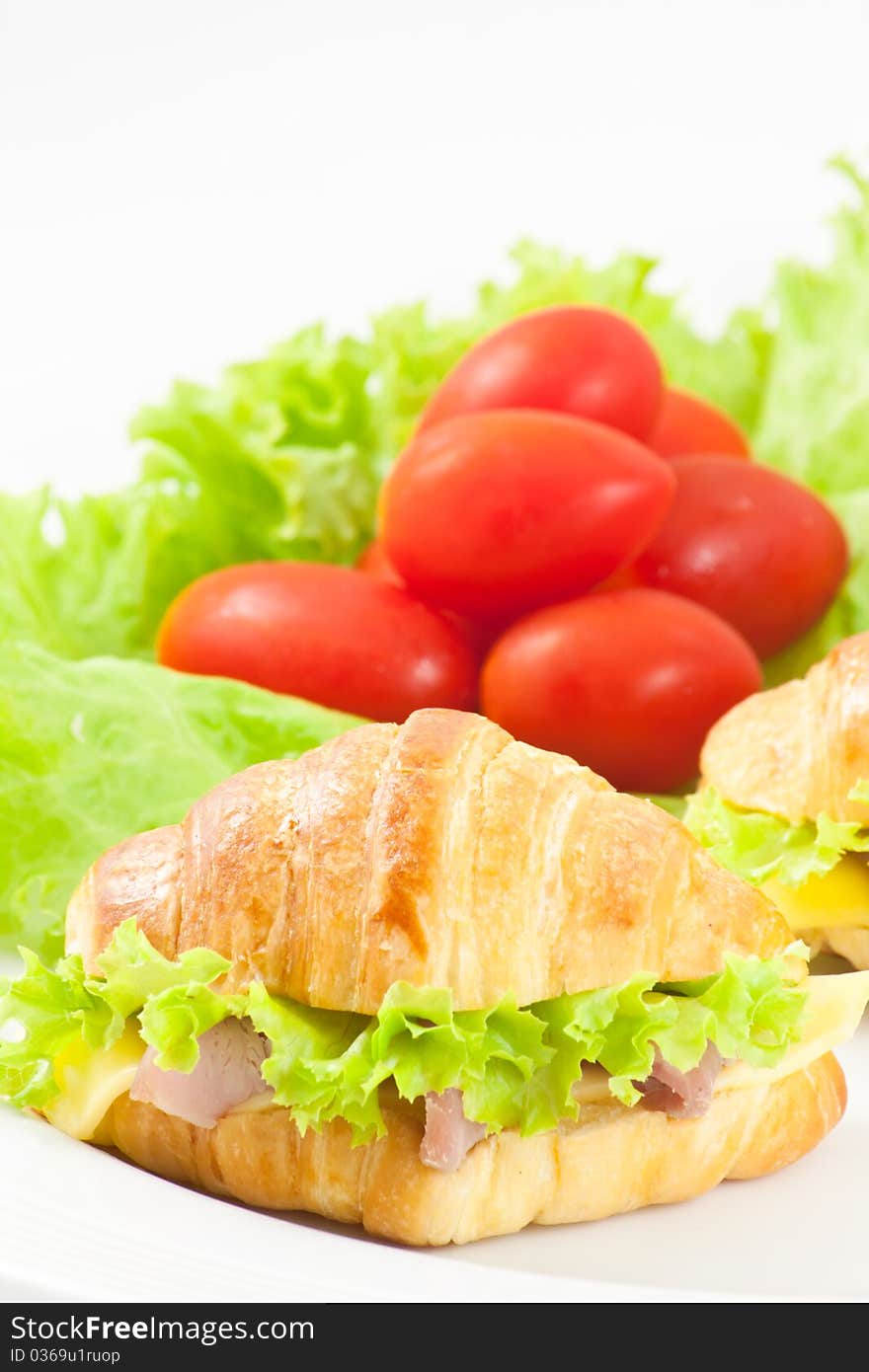 Ham and cheese croissant sandwich with tomato and lettuce in background