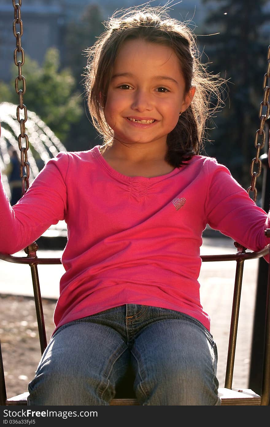 Portrait of smiling little girl on swing playground outdoors - looking at the camera