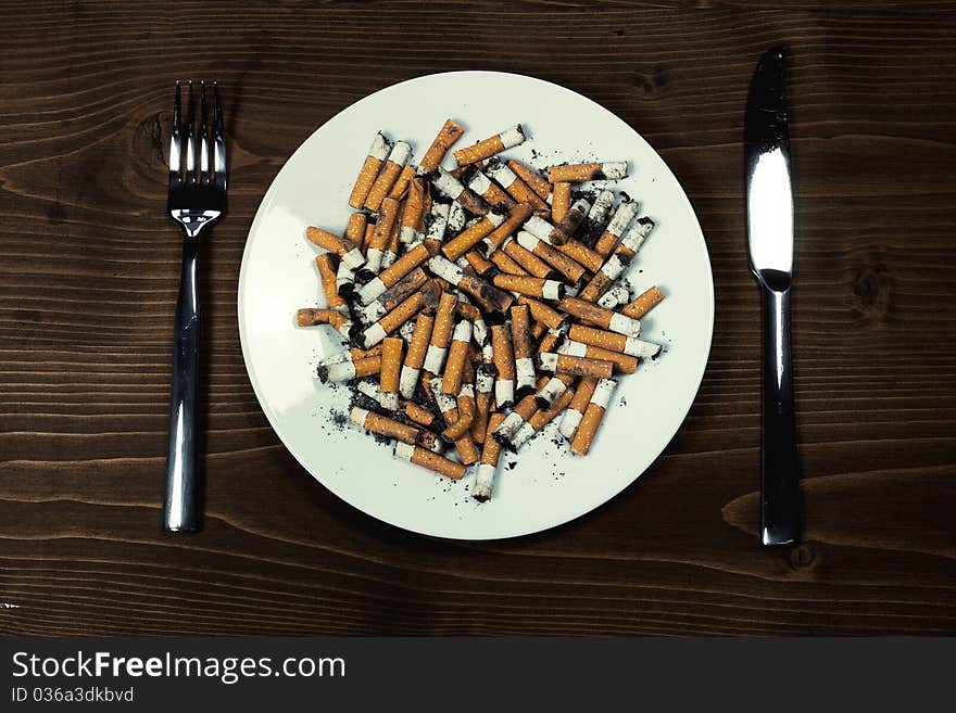 Plate with cigarettes stubs with cutlery on wood desk