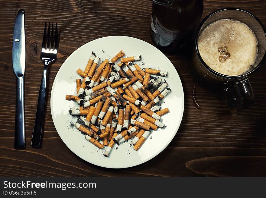 Plate with cigarettes stubs with fork and beer