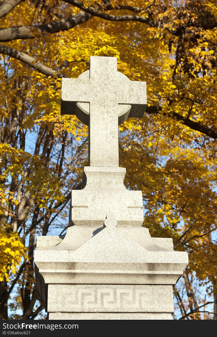 A cemetery cross monument with fall background, selective focus. A cemetery cross monument with fall background, selective focus