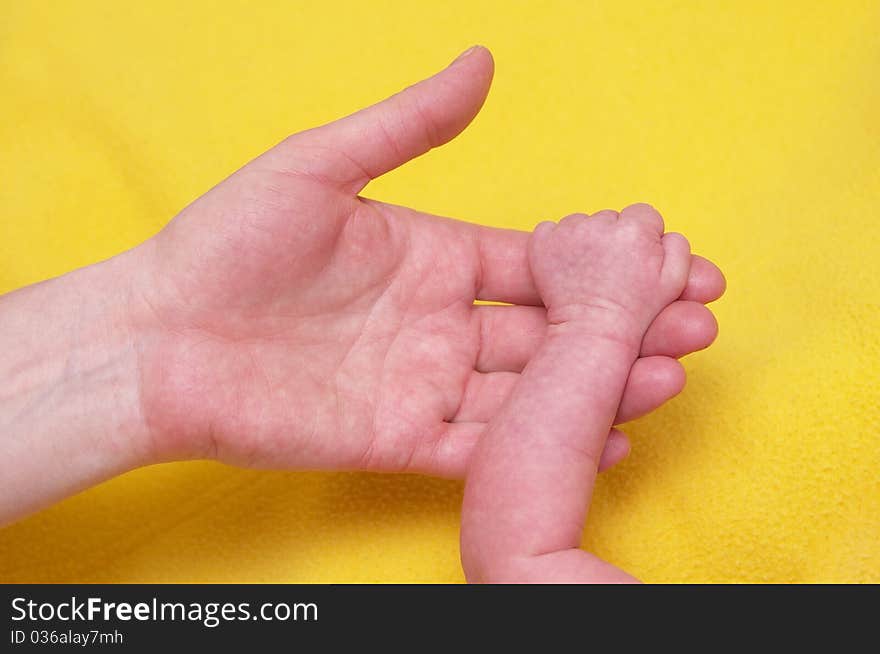 Newborn baby holding mother's hand over yellow towel. Newborn baby holding mother's hand over yellow towel