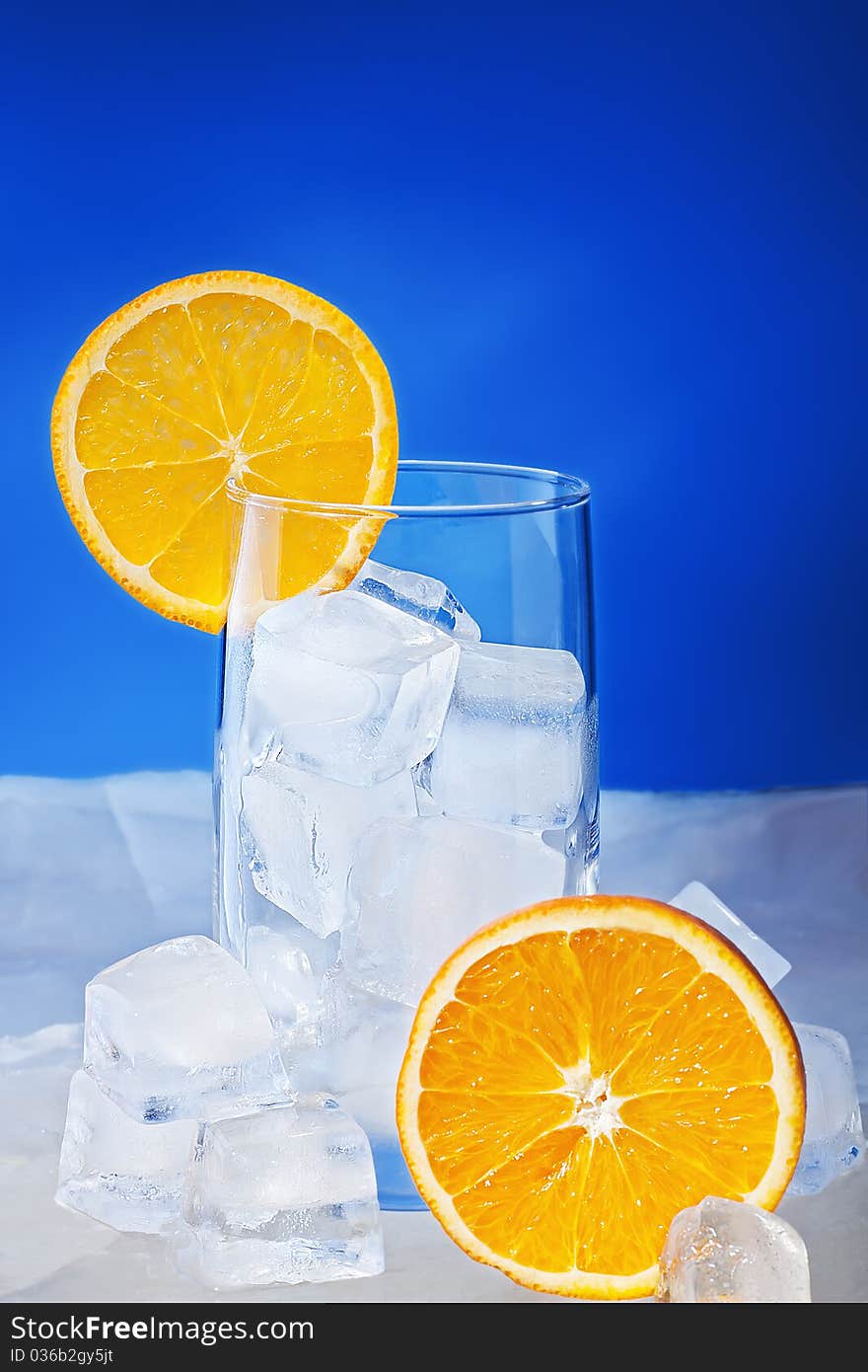 Empty Glass with orange slices stand on ice plate and it is surrounded by ice cubes.