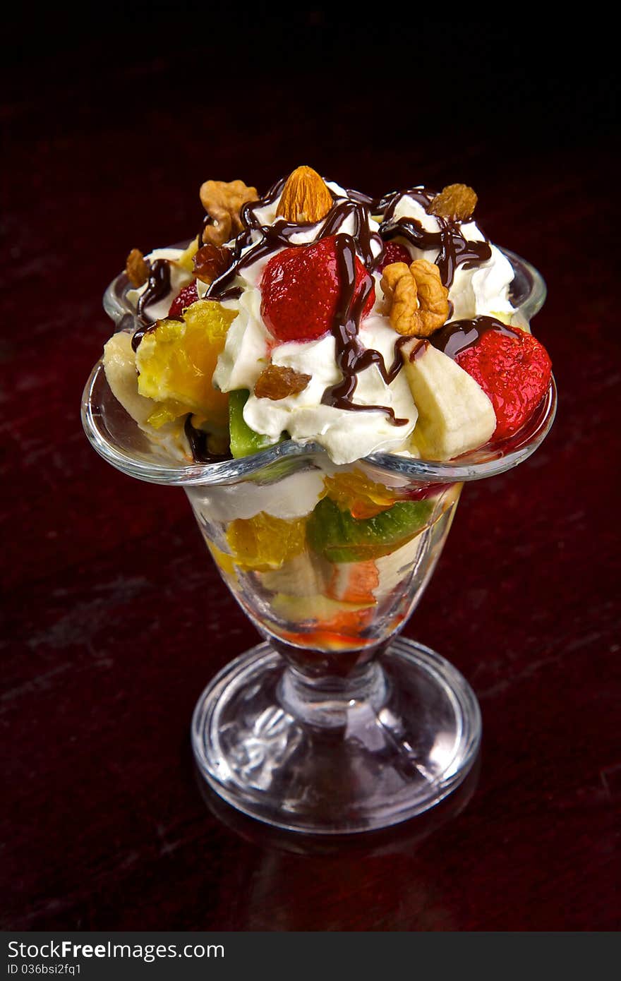 Fresh fruit in cream. A dessert from fruit and cream. Walnuts, a strawberry, a kiwi, pineapple, an apple, a banana, an orange in cream with chocolate