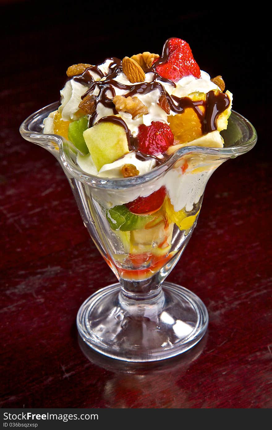 Fresh fruit in cream. A dessert from fruit and cream. Walnuts, a strawberry, a kiwi, pineapple, an apple, a banana, an orange in cream with chocolate