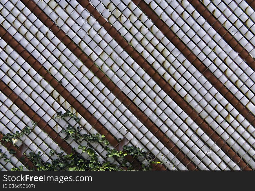 A chain link fence with striped covering and a vine.