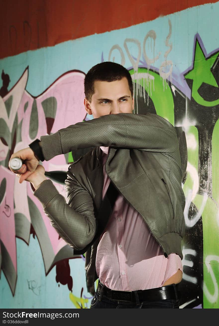 Young man choping with baseball bat against graffiti wall