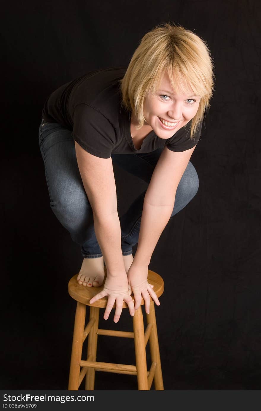 Blond woman on wooden stool crouched down and smiling. Blond woman on wooden stool crouched down and smiling.