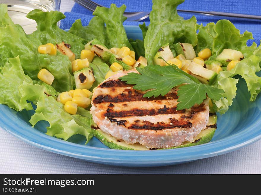 Grilled salmon and zucchini with salad and corn over a light blue plate. Studio shot