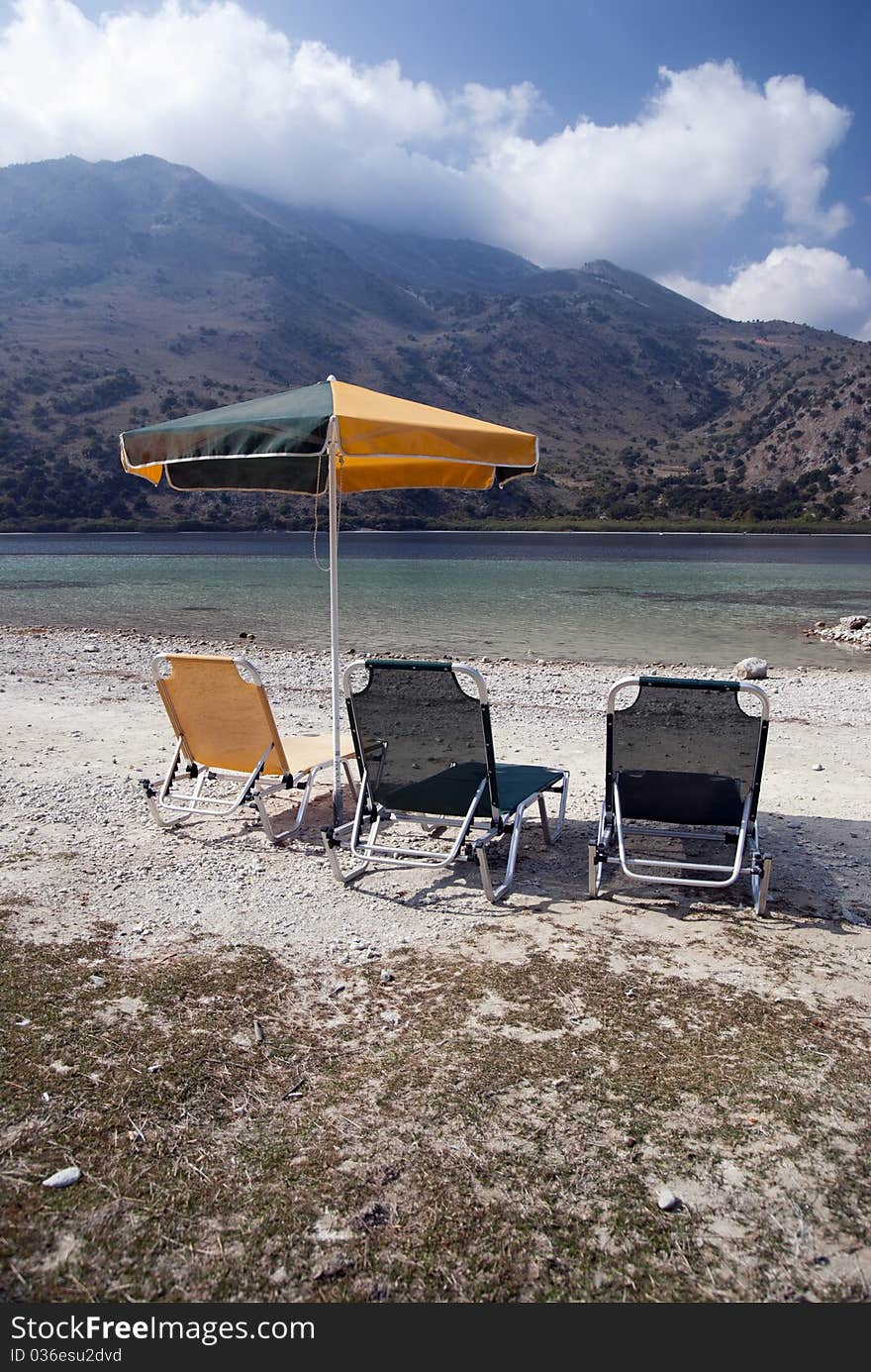 Three deck chairs and umbrellas on the background of the sea and mountains