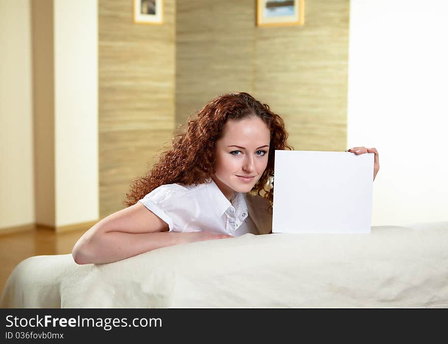 Young red hair woman sitting on a sofa and holding a white blank card. Young red hair woman sitting on a sofa and holding a white blank card