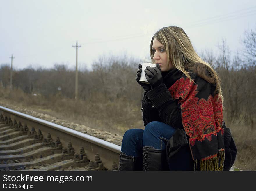 The girl drinks hot tea sitting on rails. The girl drinks hot tea sitting on rails