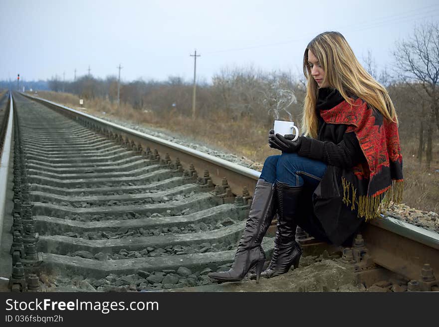The girl sits on rails and holds a cup of hot tea. The girl sits on rails and holds a cup of hot tea