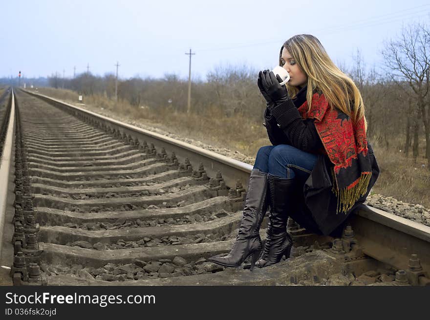 The girl sits on rails and drinks hot tea. The girl sits on rails and drinks hot tea