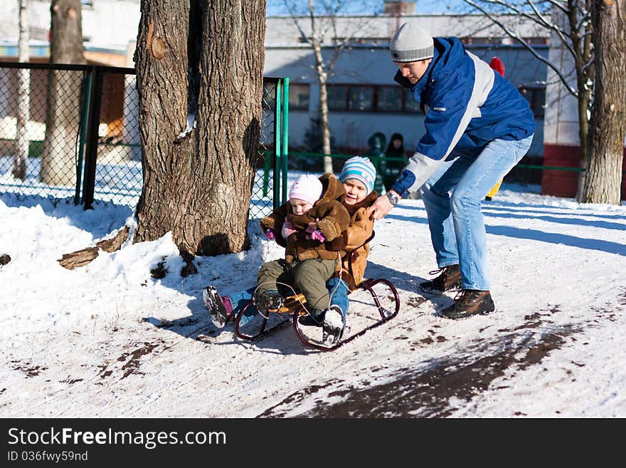 Father Pushing Children Down The Hill In A Sled