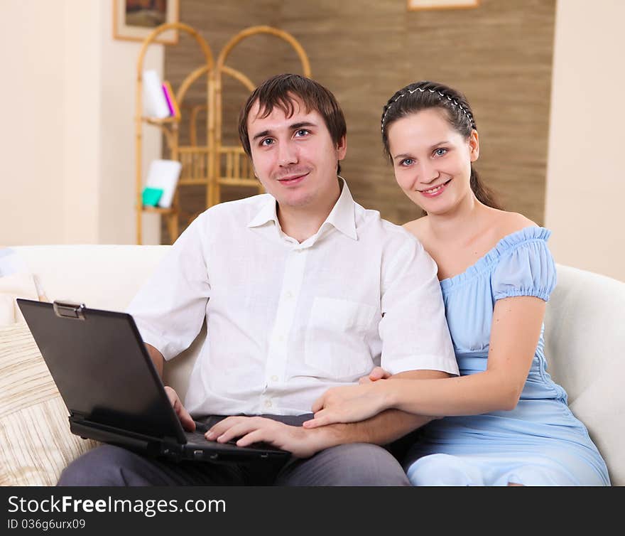 Young couple working on a laptop computer sitting on the sofa at home. Young couple working on a laptop computer sitting on the sofa at home