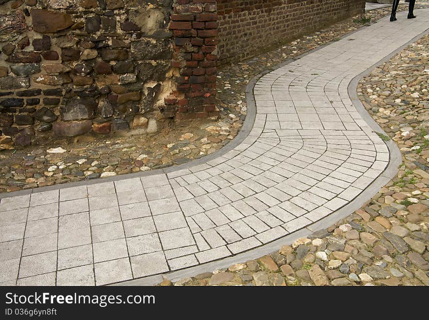 A modern grey path in an ancient surrounding of stones, someone is following the pathway. A modern grey path in an ancient surrounding of stones, someone is following the pathway