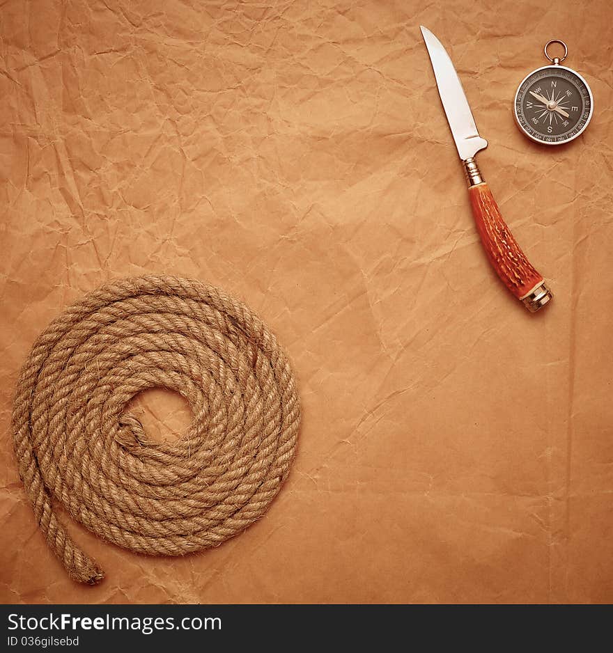 Hunting knife, rope and compass on old paper background