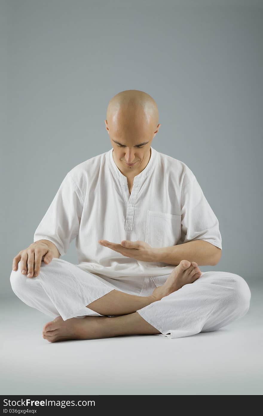 Male dressed in white sitting in meditation position, looking down. Male dressed in white sitting in meditation position, looking down