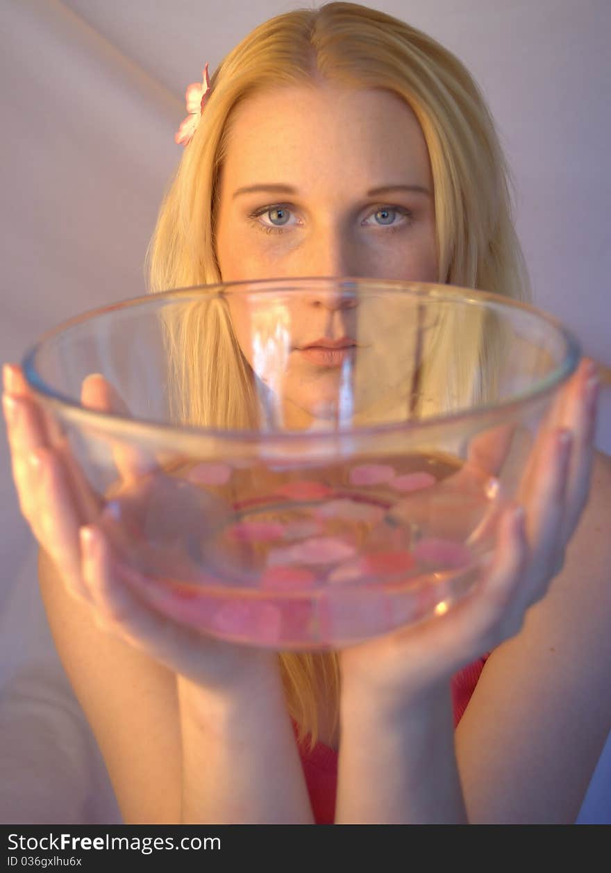 Young woman holding a glass bowl filled with water and pink petals. Young woman holding a glass bowl filled with water and pink petals