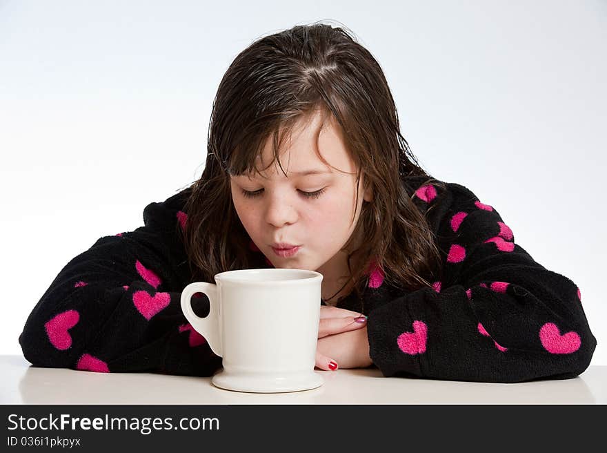 A girl in a heart bathrobe blows into a cup of hot chocolate to cool. A girl in a heart bathrobe blows into a cup of hot chocolate to cool.