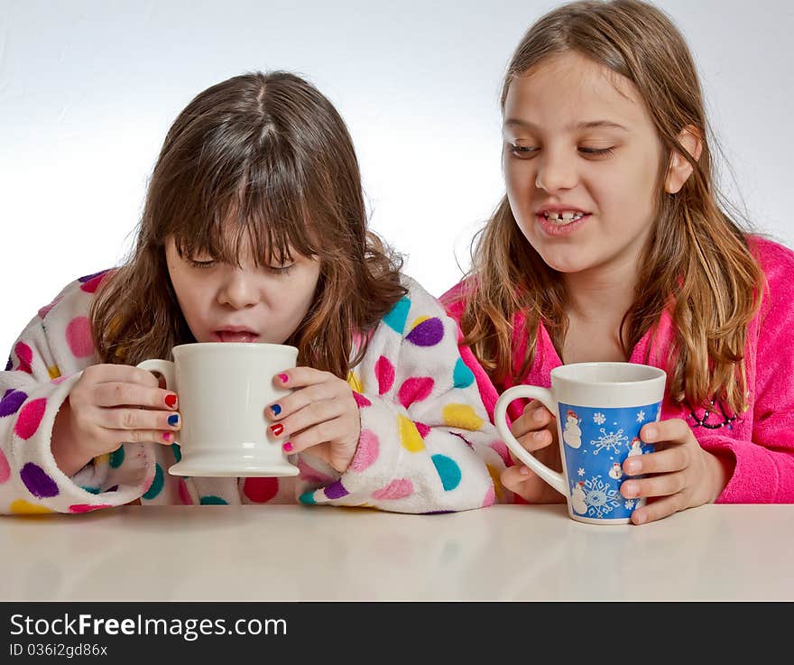 A girl looks on as one tastes her drink from a mug. A girl looks on as one tastes her drink from a mug.